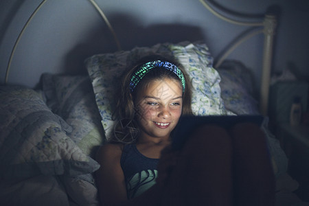 夜晚床上使用数字平板电脑的女孩图片