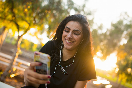 青年妇女户外戴耳机手持智能的青年妇女图片