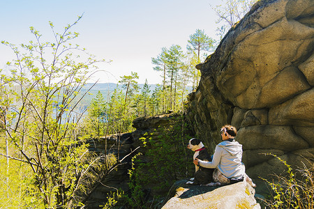 女远足者和她的斗牛犬坐在山岩上看着森林俄罗斯图片