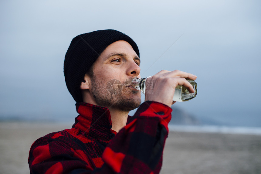 海滩上的成年男性饮用瓶装水图片