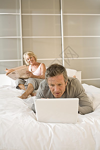 床上阅读报纸和使用笔记本电脑的夫妇图片
