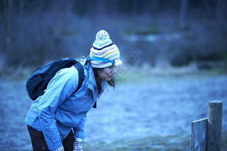 黄昏时分一名手持手电筒的女徒步旅行者在森林里阅读告示图片