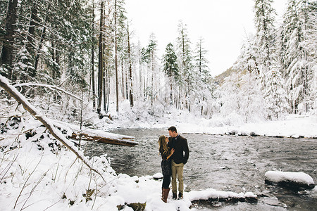 在雪覆盖的森林里一对情侣面朝河微笑两个人高清图片素材