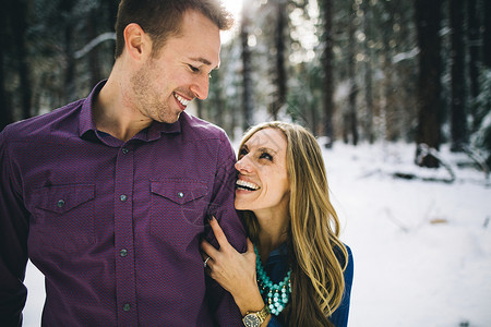 在雪覆盖的森林中拥抱和微笑的情侣图片