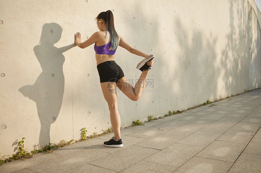 运动女青年靠墙拉伸大腿图片