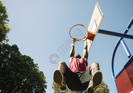 年轻男篮球运动员挂在篮球框上图片