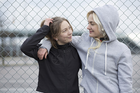 两个快乐的女孩倚着铁丝栅栏聊天背景图片