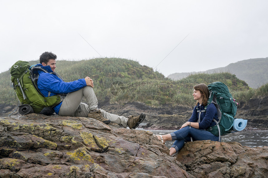 背着包的年轻夫妇坐在岩石上图片