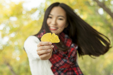 秋天公园中手拿黄金叶的年轻女子肖像图片