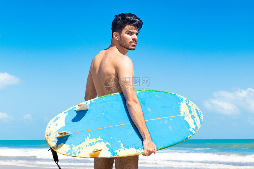 年轻人站在海滩上举着冲浪板巴西塞阿拉福塔莱萨图片