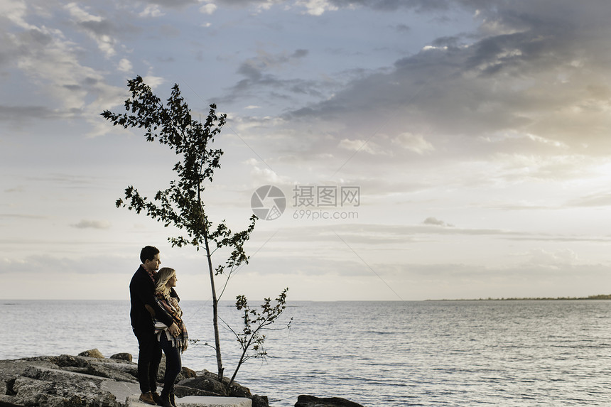 年轻夫妇站在海边的岩石上看着风景图片