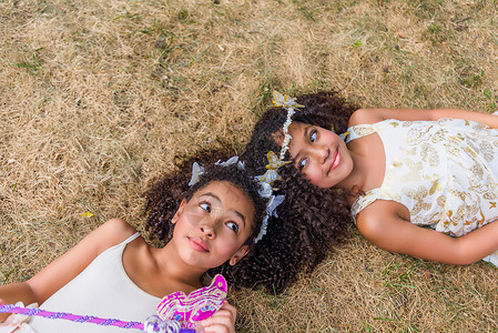 两个女孩打扮成仙女头挨头躺在草地上蝴蝶高清图片素材