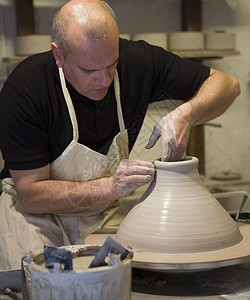 在车间陶器轮上制做陶罐的男陶工背景图片