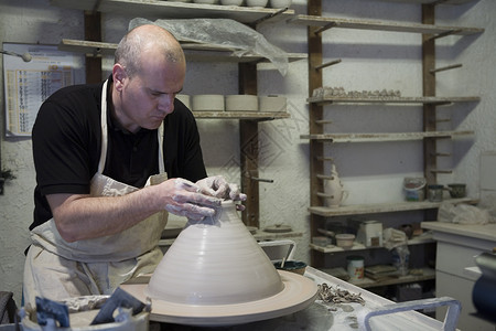 在车间陶器轮上制做陶罐的男陶工背景图片
