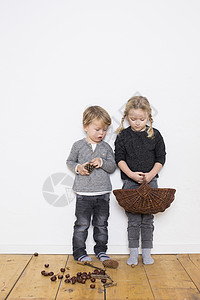 年轻的女孩和男孩女孩拿着柳条篮男孩拿着松果松果和锥在地板上图片