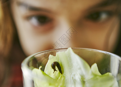 仔细端详菜叶上的鼻涕虫的女孩的眼部特写图片