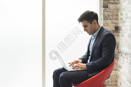 坐在办公椅子上用笔记本电脑打字的商人图片