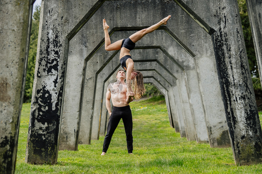 在混凝土桥下练瑜伽的年轻女人在男的双手上平衡图片
