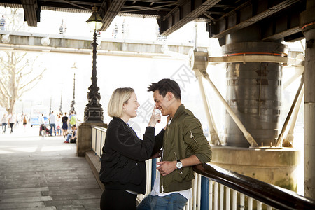 年轻夫妇站在桥下年轻女人摸着男人的脸微笑图片