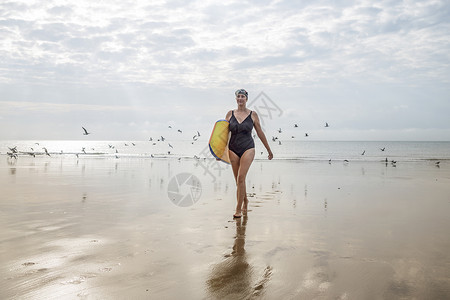 在联合王国海滩上拿着冲浪板的妇女图片