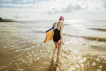 在联合王国的海上拿着冲浪板的年轻妇女图片