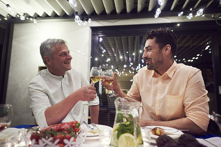 两个男人坐在晚餐桌边拿着红酒杯做吐司中年男子高清图片素材