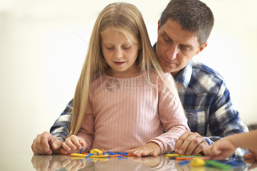 父亲和女儿坐在桌边玩泥土模拟游戏图片