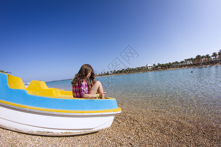 坐在沙滩小船的女孩屈膝远望图片