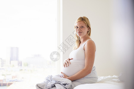 怀孕的年轻妇坐在床上手摸着肚子图片