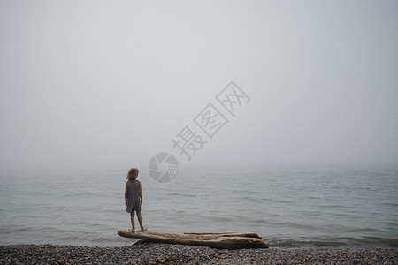 女孩站在漂浮木上看着大海高清图片