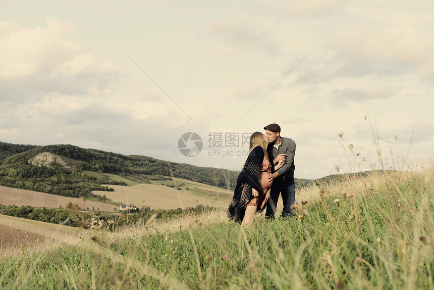 浪漫的怀孕中年夫妇在乡村山坡上接吻图片