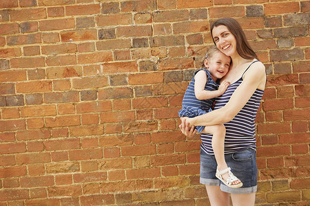 怀孕的中年成妇用砖墙抱着女儿的肖像图片