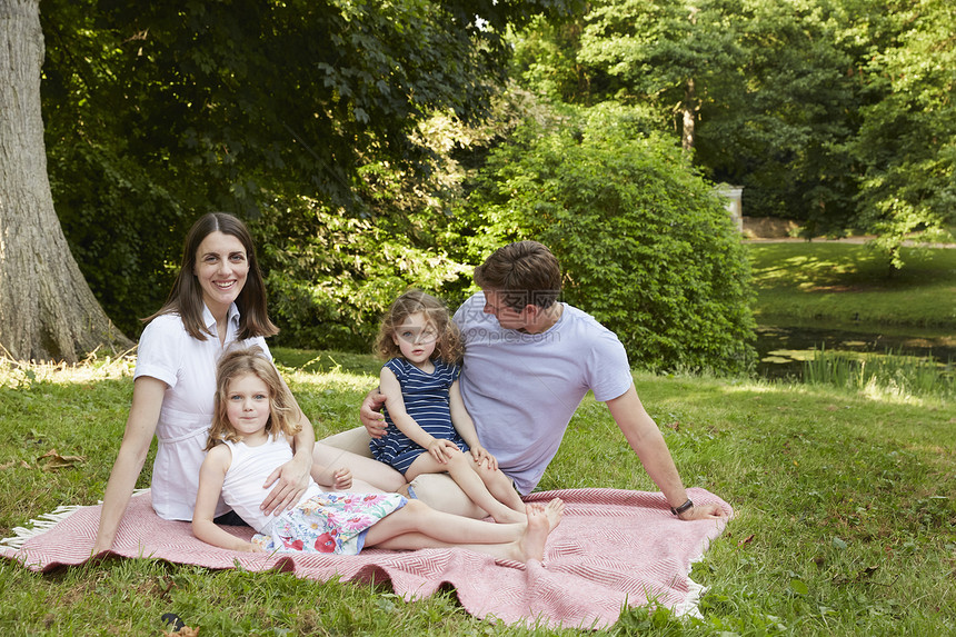 在公园野餐毯上对中成年父母和两个女儿的肖像图片