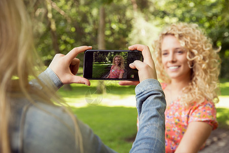 使用智能手机拍摄朋友照片的妇女图片