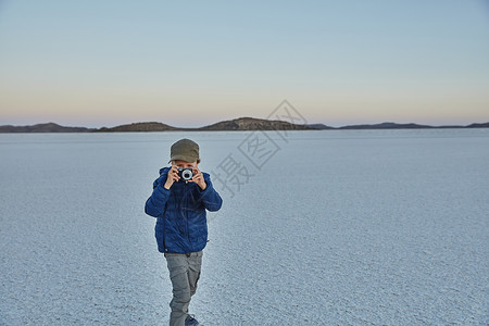 青年男孩站在盐滩上拿着相机拍照图片