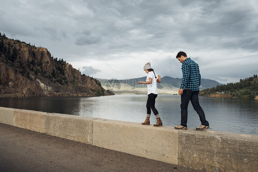 在美国科罗拉多州湖边墙上一前一后行走的情侣图片