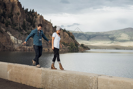 在美国科罗拉多州湖边墙上一前一后行走的情侣图片