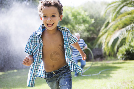 花园里男孩在拿着喷水管的爷爷前面跑图片