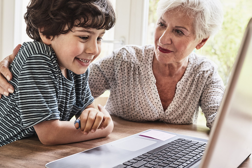 坐在桌上使用笔记本电脑的祖母和孙子图片