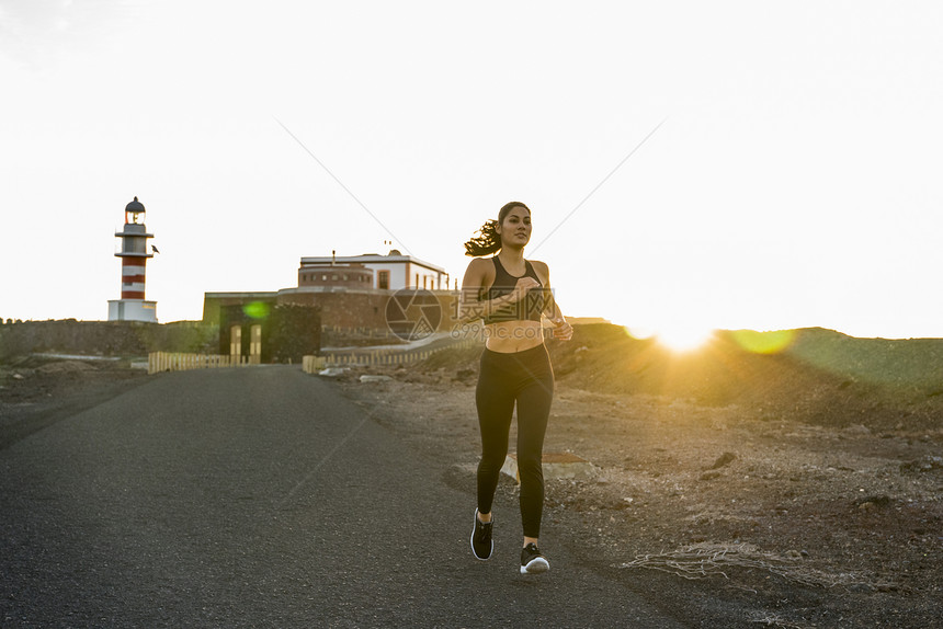西班牙加那利群岛拉斯帕尔马市日落时在农村公路上奔向的年轻女跑者图片
