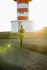 年轻女跑者在日落时沿海泥土轨道上奔跑背景图片