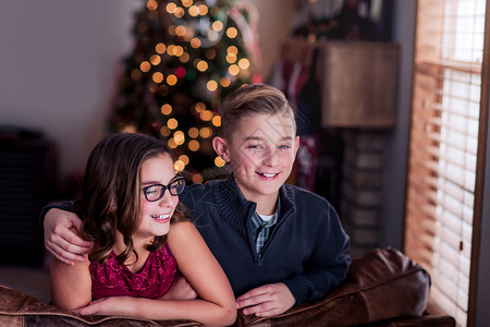 在圣诞树背景下靠在沙发上笑着的兄弟姐妹们图片