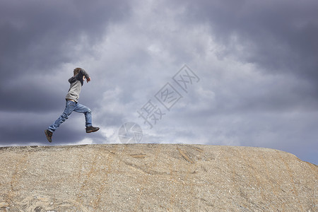 暴风雨前的天空下男孩在岩石顶上奔跑无忧无虑的高清图片素材