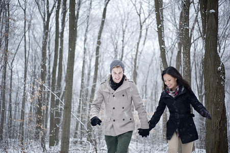 在加拿大安略省雪覆盖的森林中手牵行走的年轻夫妇针织帽高清图片素材