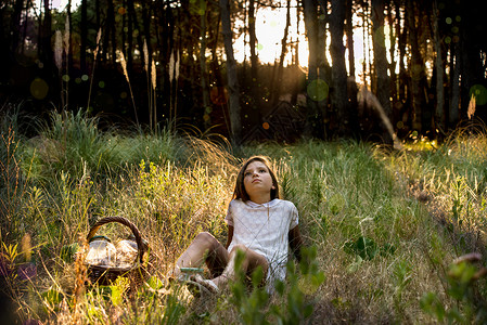 有野餐篮子的女孩在日光森林向上仰望休闲服高清图片素材