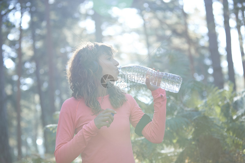年轻的女慢跑者在日光林饮用瓶装水图片