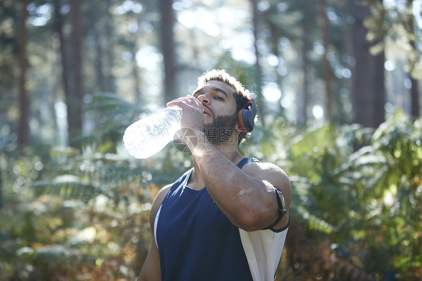 日光林中男跑者饮用瓶装水图片