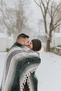 在雪地的风景下包着毯子接吻的一对夫妇加拿大乔治敦白天高清图片素材