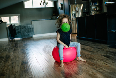 真人小女孩家里坐在健身球上嘴里叼着气球的小女孩背景
