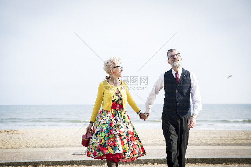 打扮复古的老年夫妻手牵手在海滩上漫步图片